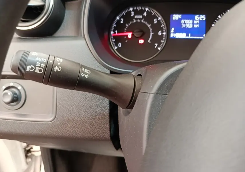 Gros plan sur le tableau de bord noir du Dacia Duster blanc, avec compte-tours et écran multifonctions bleu allumé.
