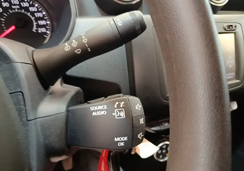 Gros plan sur le volant cuir synthétique du Dacia Duster blanc, avec commandes audio intégrées visibles.