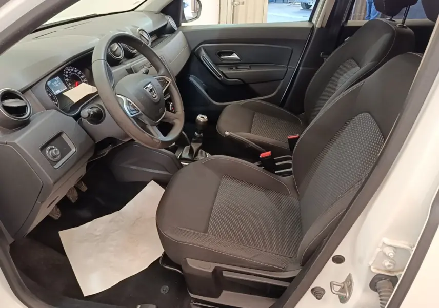 Vue intérieure côté conducteur du Dacia Duster blanc 2021, volant multifonctions cuir synthétique et sièges tissu noirs.