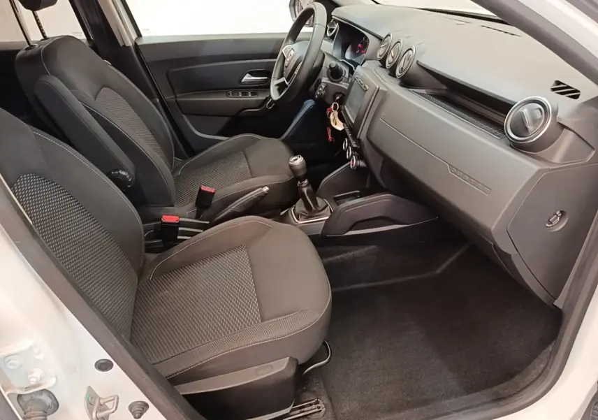 Vue intérieure côté conducteur du Dacia Duster blanc 2021, montrant sièges noirs, volant multifonctions et tableau de bord épuré.