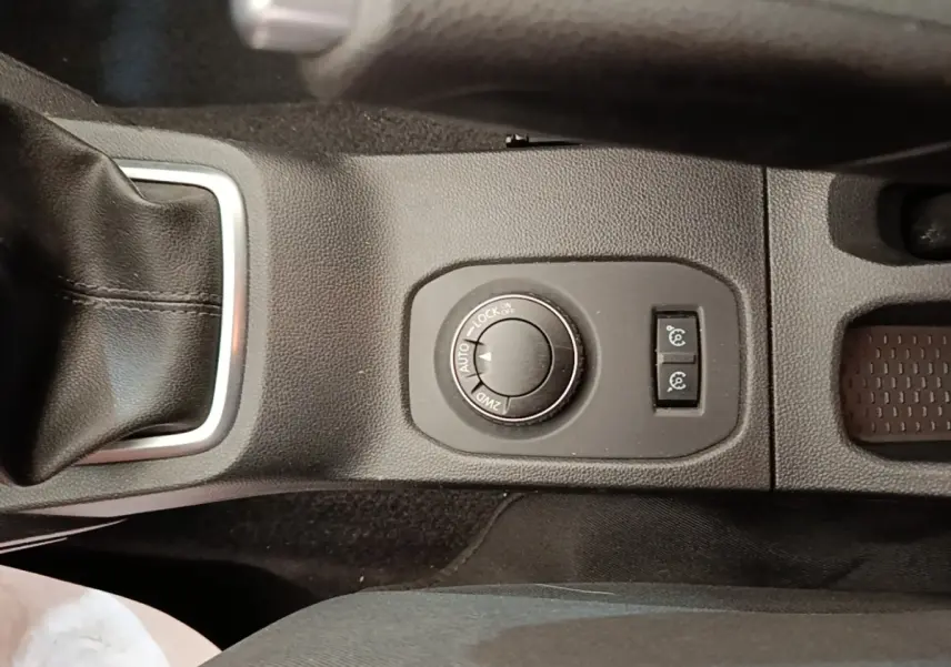 Gros plan sur la molette de sélection 4x4 et les boutons de contrôle sur la console centrale noire du Dacia Duster blanc.