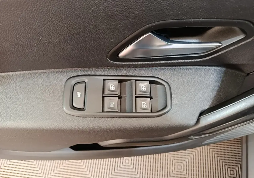 Gros plan sur la commande des vitres électriques et la poignée intérieure côté conducteur du Dacia Duster blanc.