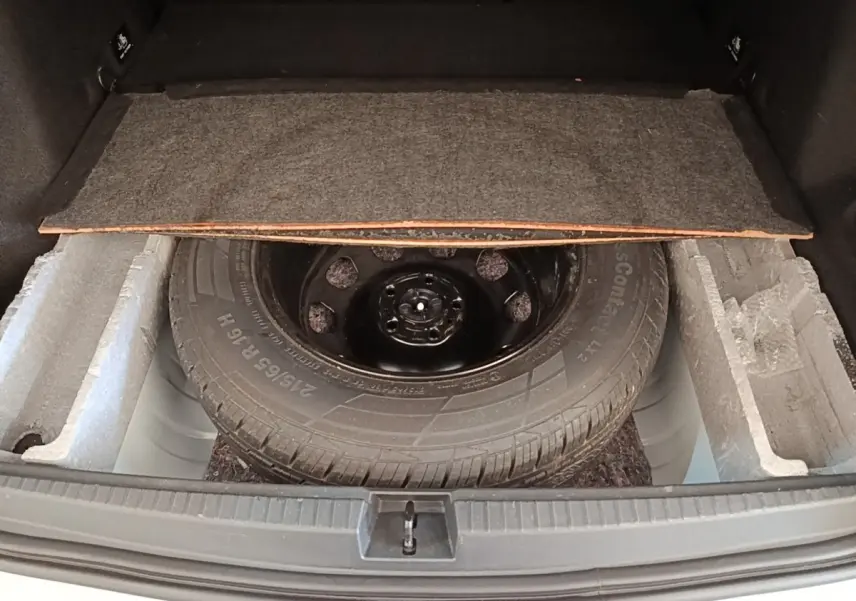 Vue du coffre ouvert d'un Dacia Duster blanc, montrant la roue de secours et le compartiment de rangement sous la tablette.