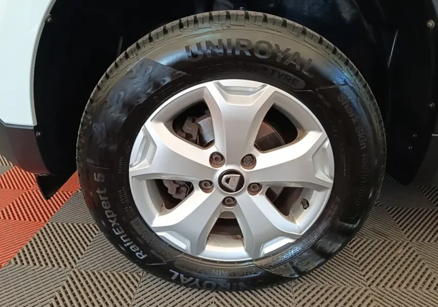 Gros plan sur la roue avant gauche d'un Dacia Duster blanc avec jante argentée et pneu Uniroyal RainExpert 5.