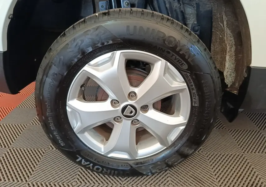Gros plan sur la roue avant gauche du Dacia Duster blanc, mettant en valeur la jante argentée et le pneu Uniroyal.