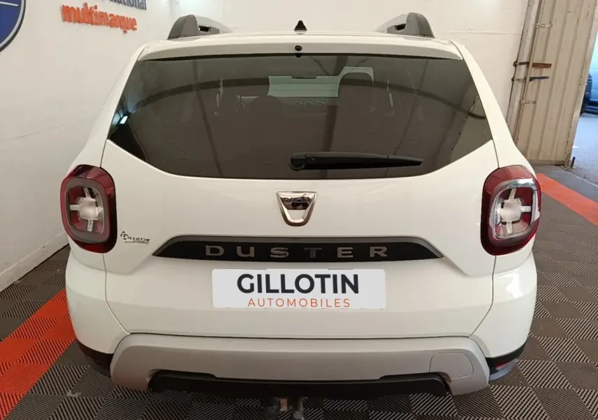 Vue arrière d'un Dacia Duster blanc 2021 avec feux carrés et attelage visible dans un garage.