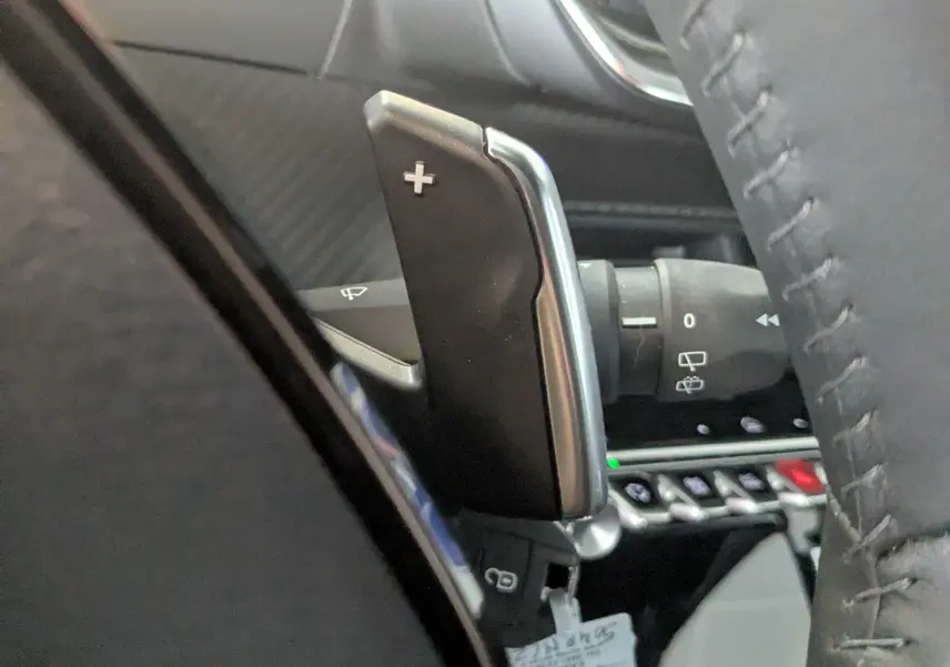 Gros plan sur la palette de changement de vitesse + au volant du Peugeot 2008 Hybrid 145, intérieur noir.