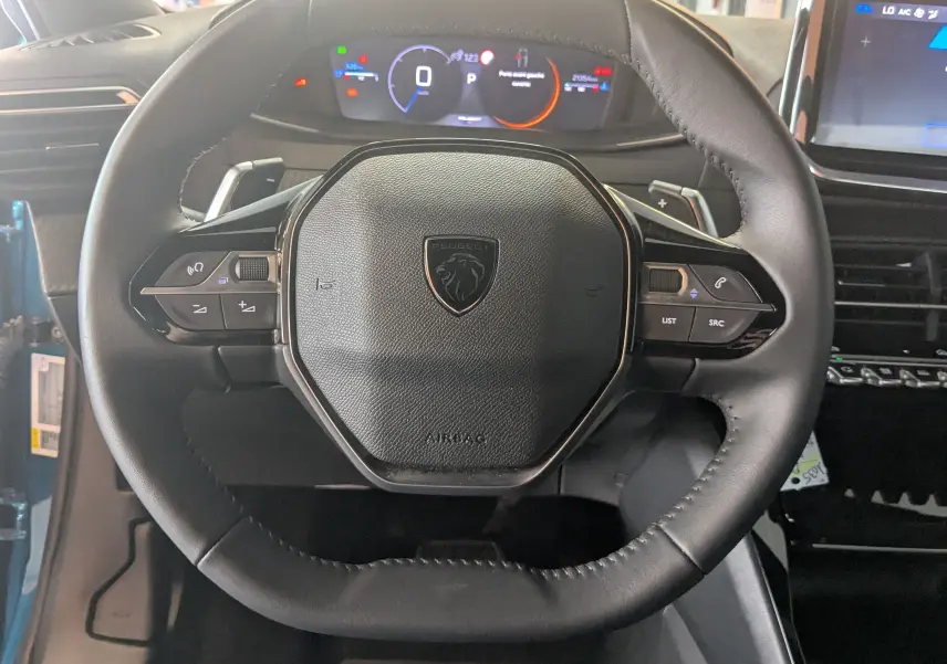 Vue rapprochée du volant cuir noir du Peugeot 2008 Hybrid 145 avec commandes intégrées et tableau de bord numérique.