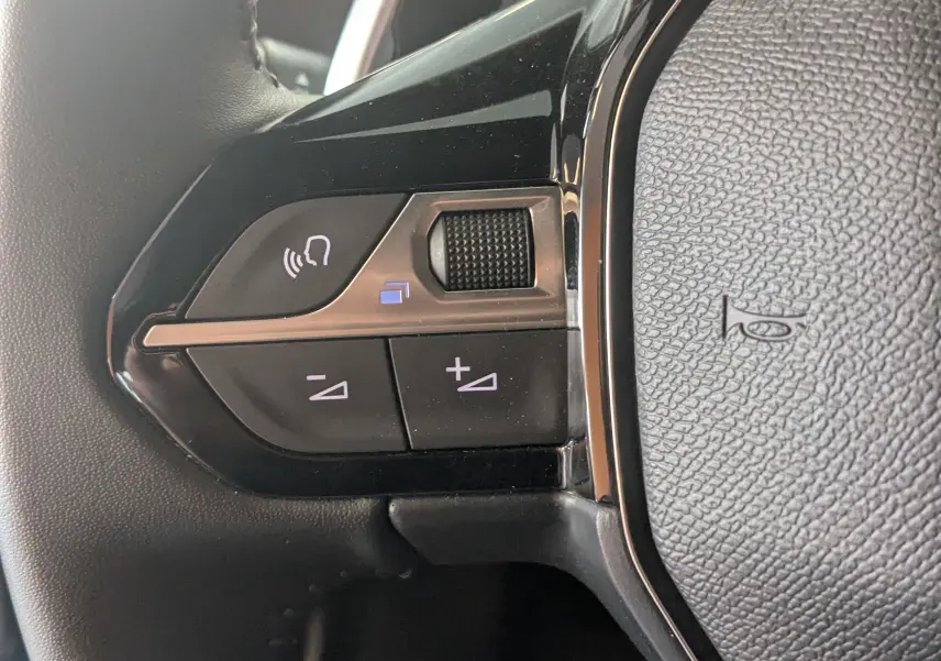 Gros plan sur les commandes de volume au volant noir du Peugeot 2008 Hybrid 145 e-DCS6 Allure, finition tissu gris-noir.