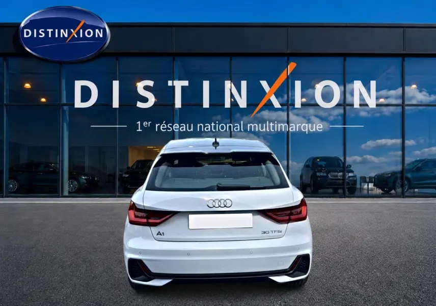 Vue arrière d'une Audi A1 Sportback blanche avec feux LED et becquet, stationnée devant une vitrine Distinxion.