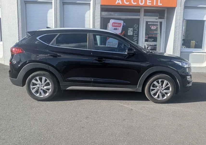 Vue de profil côté gauche d'un Hyundai Tucson noir garé devant un bâtiment avec enseigne Distinxion.