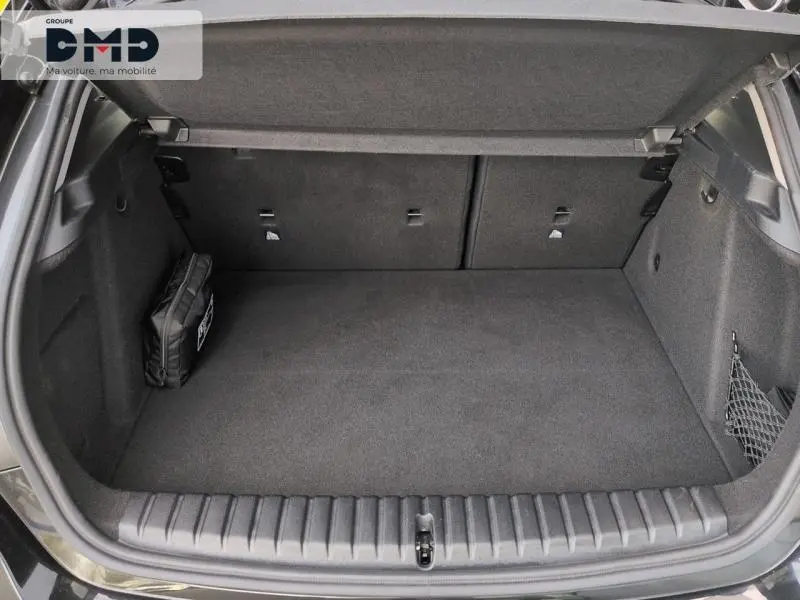 Vue intérieure du coffre ouvert d'une BMW Série 1 118iA 2024 en Saphirschwarz métallisé, avec tapis et filet de rangement.
