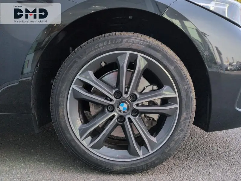 Gros plan sur la jante alu grise et le pneu Michelin d'une BMW Série 1 118iA Saphirschwarz métallisé, côté avant droit.
