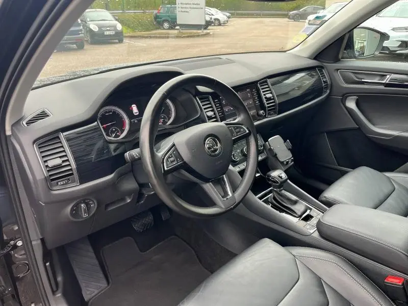 Vue intérieure côté conducteur du Skoda Kodiaq noir Magic Nacré, tableau de bord moderne avec volant cuir multifonction et écran tactile.