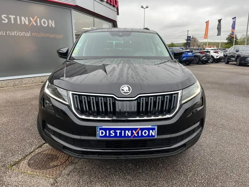 Vue frontale d'un SKODA KODIAQ noir Magic Nacré avec calandre chromée et phares LED allumés, sous un ciel nuageux.