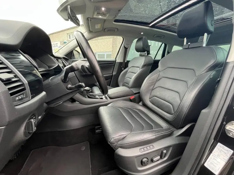 Vue intérieure côté conducteur du Skoda Kodiaq noir Magic Nacré, sièges cuir noir, volant multifonction et toit panoramique ouvert.