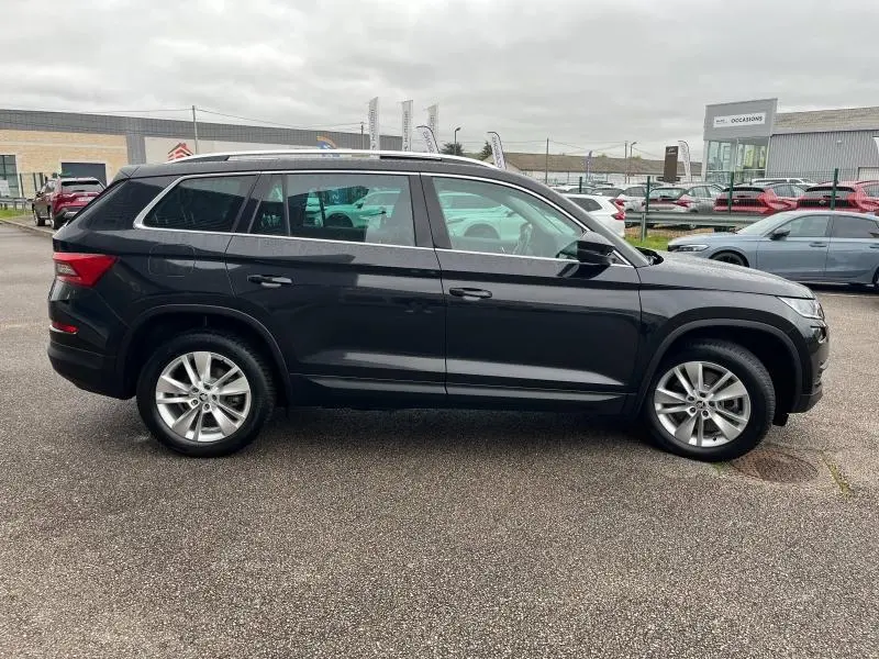 Vue de profil côté gauche d'un SUV SKODA KODIAQ noir Magic Nacré, avec jantes alliage et barres de toit argentées.