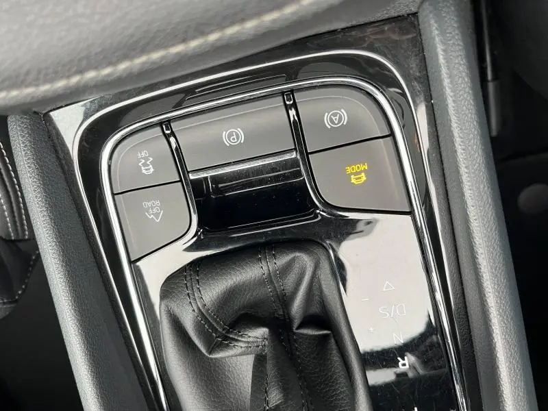 Gros plan sur la console centrale noire avec levier de vitesses cuir et boutons de contrôle du mode de conduite et frein à main électrique.