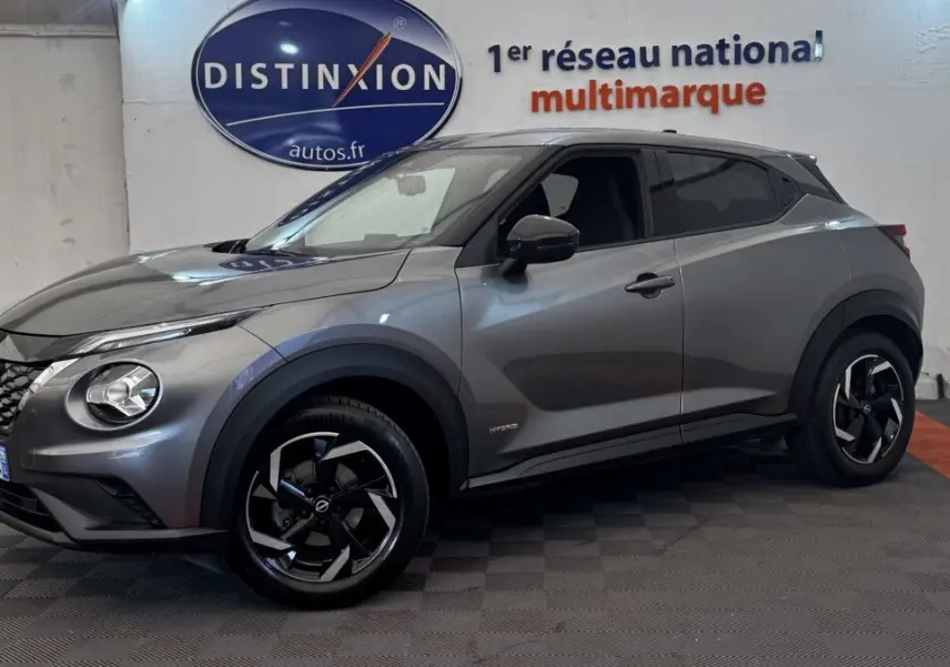 Nissan Juke Hybrid gris foncé vu de profil droit en intérieur, avec jantes noires et détails hybrides visibles.