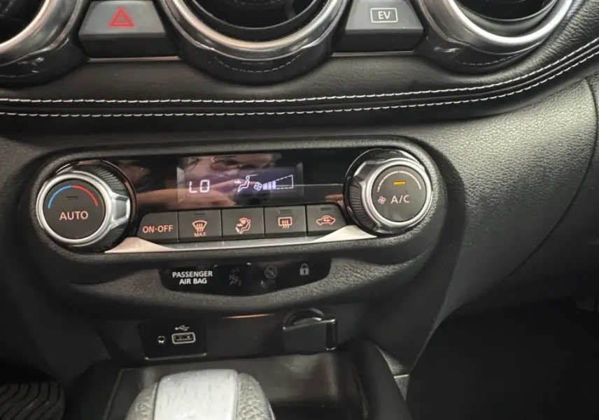 Gros plan sur la console centrale noire du Nissan Juke Hybrid 143 Business+ 2023 avec commandes climatisation et ports USB.