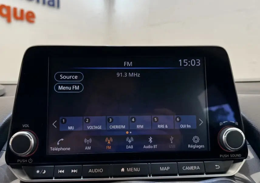 Écran tactile central du Nissan Juke Hybrid 2023 affichant la radio FM avec commandes autour en intérieur noir.