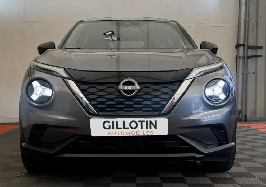 Vue frontale d'un Nissan Juke Hybrid 143 Business+ gris foncé avec phares LED allumés en intérieur.