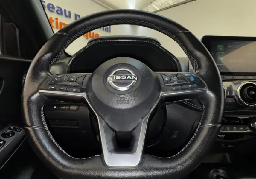 Vue intérieure centrée sur le volant cuir noir du Nissan Juke Hybrid 2023 avec écran tactile et commandes au volant.