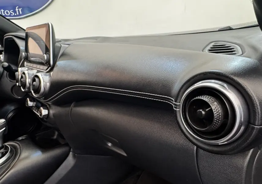 Vue intérieure côté passager du tableau de bord noir avec écran tactile et aérateurs ronds du Nissan Juke Hybrid 2023.
