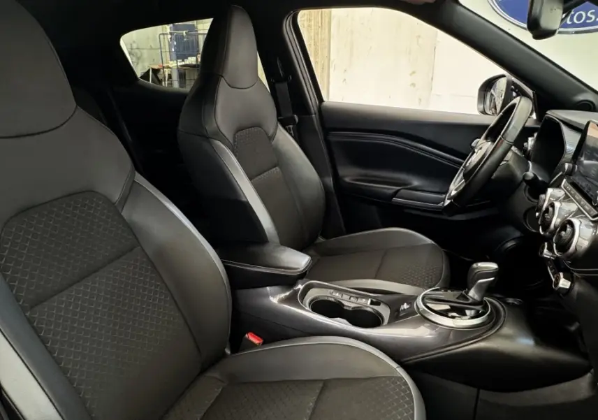 Intérieur avant du Nissan Juke Hybrid 143 Business+ 2023, sièges noirs, console centrale avec boîte auto et écran tactile.