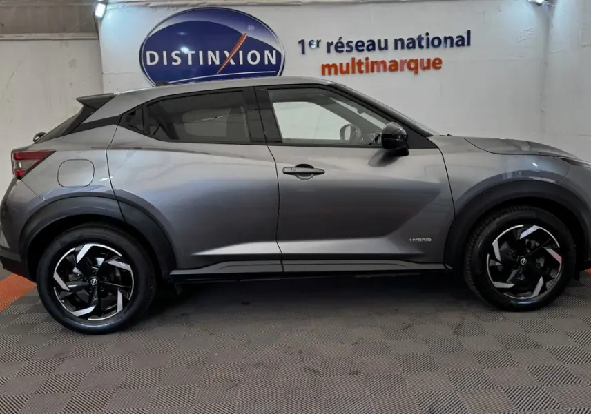 Vue latérale droite d'un Nissan Juke Hybrid 143 Business+ gris foncé avec jantes noires et logo Hybrid visible sur la porte.