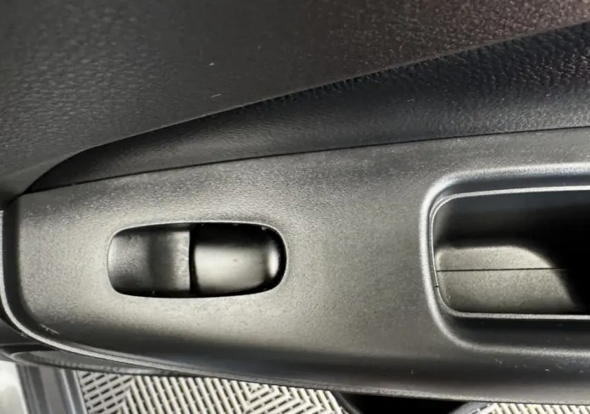 Détail de la commande de lève-vitre côté conducteur en plastique noir dans un Nissan Juke Hybrid 2023 gris foncé.