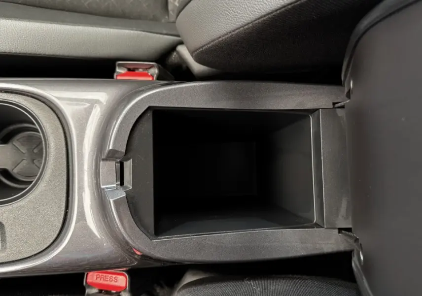 Vue rapprochée de la console centrale ouverte du Nissan Juke Hybrid 143 Business+ gris foncé, montrant le rangement intérieur.