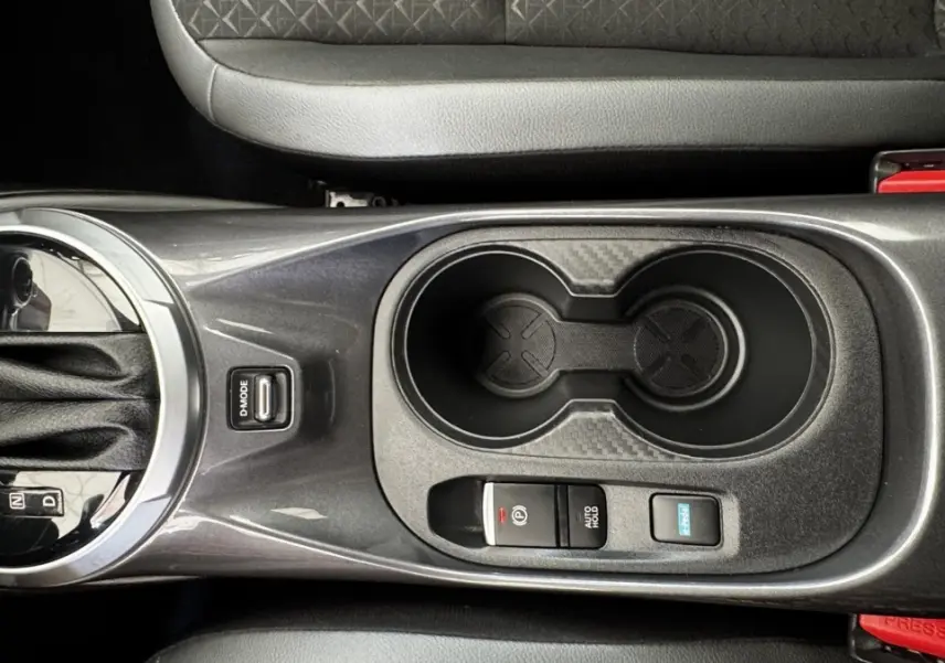 Vue plongeante sur la console centrale grise du Nissan Juke Hybrid 143 Business+ avec levier de vitesses et porte-gobelets.