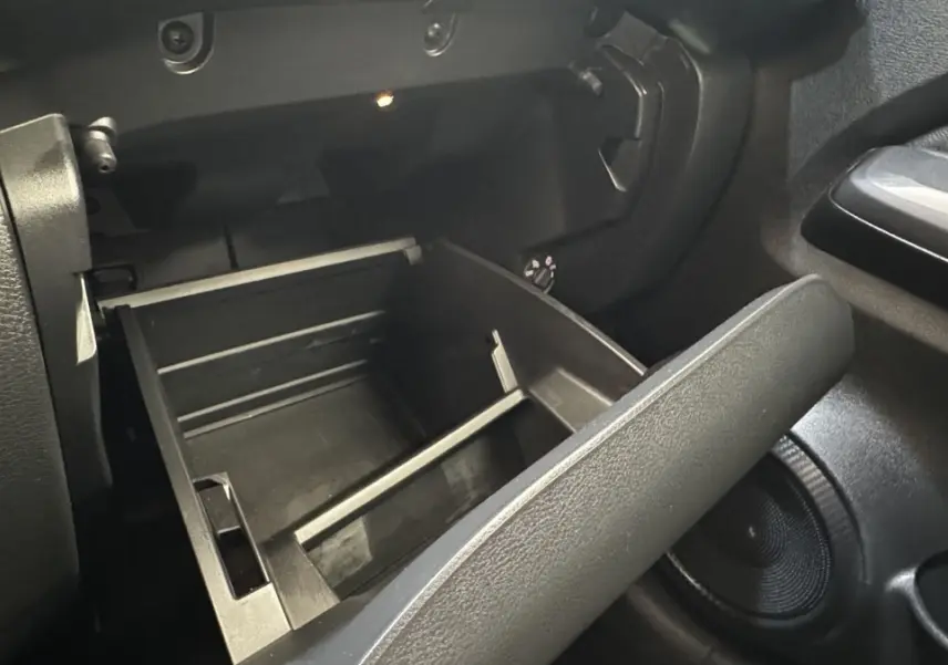 Intérieur du Nissan Juke Hybrid 143 Business+ 2023, vue sur la boîte à gants ouverte côté passager en plastique noir.