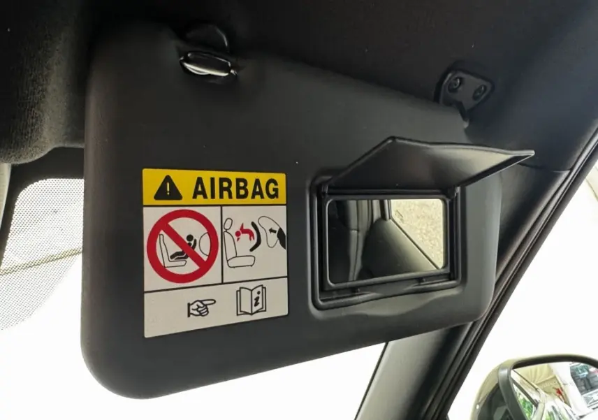 Détail du pare-soleil côté conducteur avec miroir et avertissement airbag dans un Nissan Juke gris foncé 2023.
