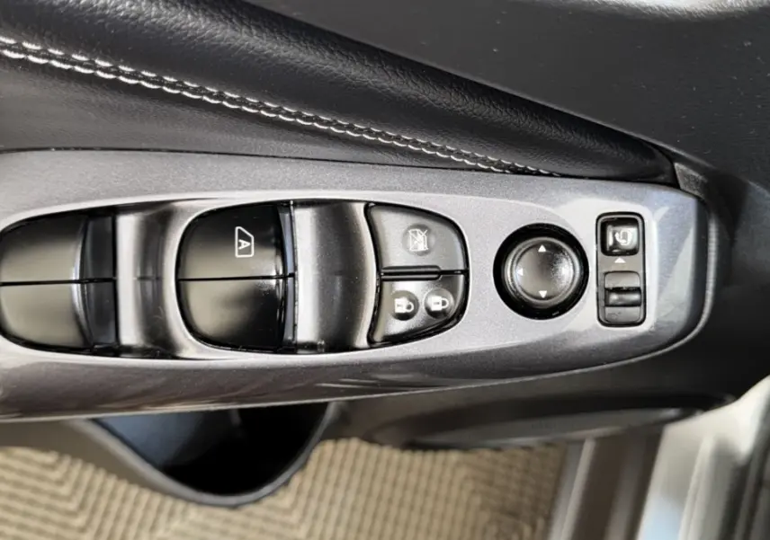 Gros plan sur les commandes de réglage des vitres et rétroviseurs côté conducteur du Nissan Juke Hybrid 143 Business+ gris foncé.