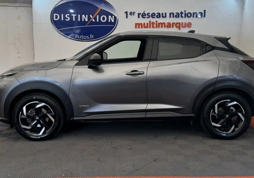Profil latéral droit du Nissan Juke Hybrid 143 Business+ gris foncé avec jantes noires et logo hybride visible.