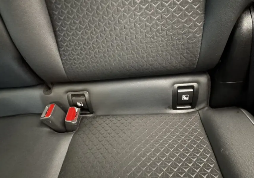 Gros plan sur la banquette arrière noire du Nissan Juke Hybrid 143 Business+ avec fixation Isofix et boucles de ceinture rouges.