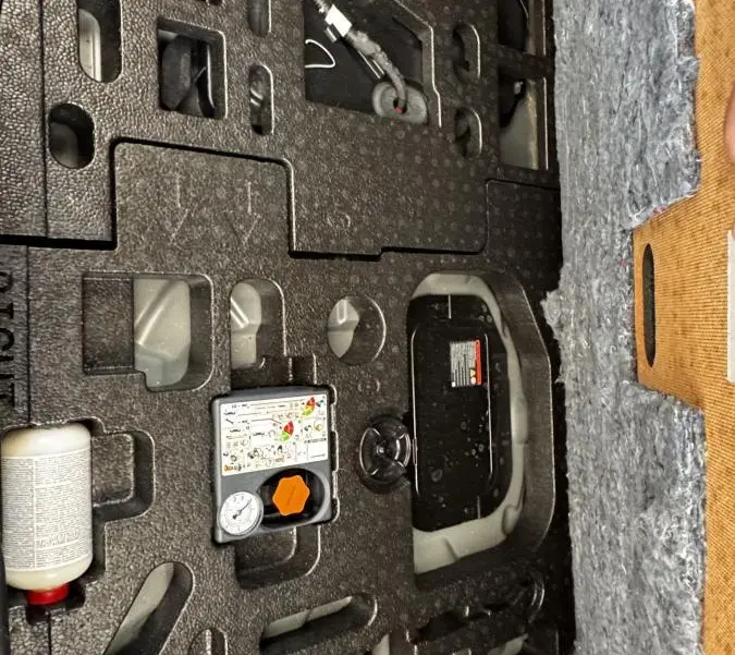 Vue rapprochée du compartiment de rangement sous le plancher du coffre du Nissan Juke Hybrid 143 Business+ gris foncé.