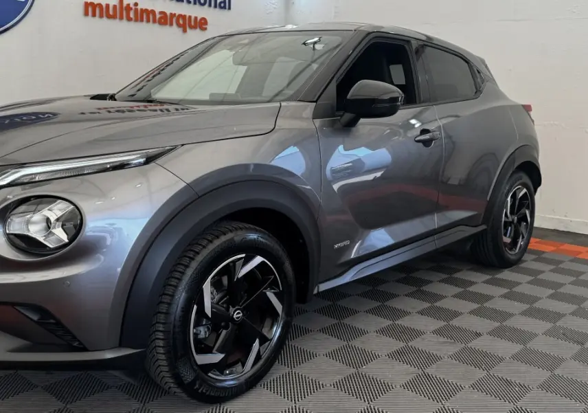 Nissan Juke Hybrid gris foncé vu de 3/4 avant droit, avec jantes noires et logo Hybrid sur la portière.