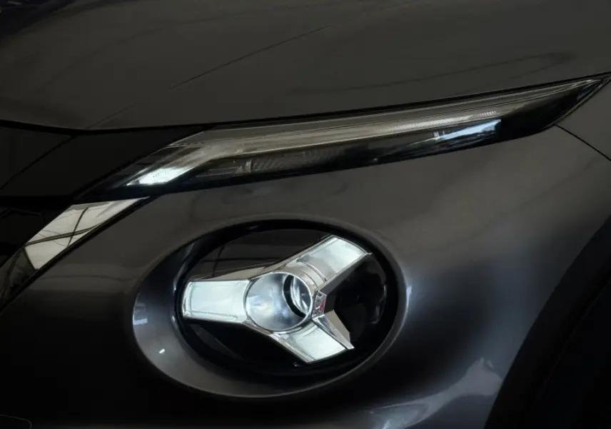 Gros plan sur le phare avant droit et le feu diurne d'un Nissan Juke Hybrid gris foncé, détails modernes et lisses.