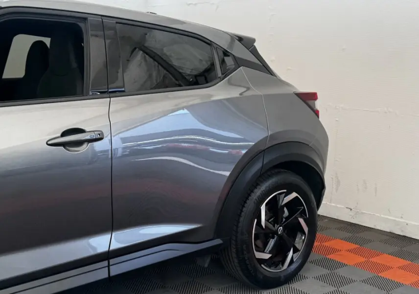 Vue côté droit arrière du Nissan Juke Hybrid 143 Business+ gris foncé avec jante noire et détails de carrosserie marqués.