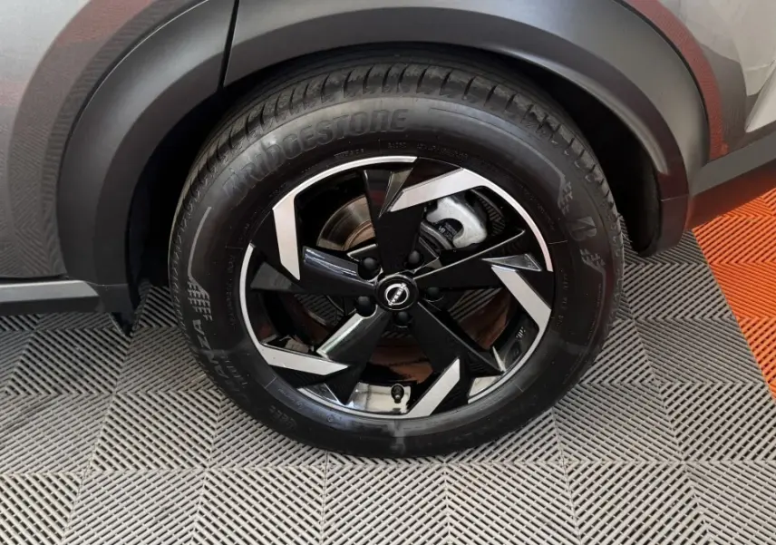 Gros plan sur la roue avant droite du Nissan Juke Hybrid gris foncé avec jante noire et argentée au design moderne.