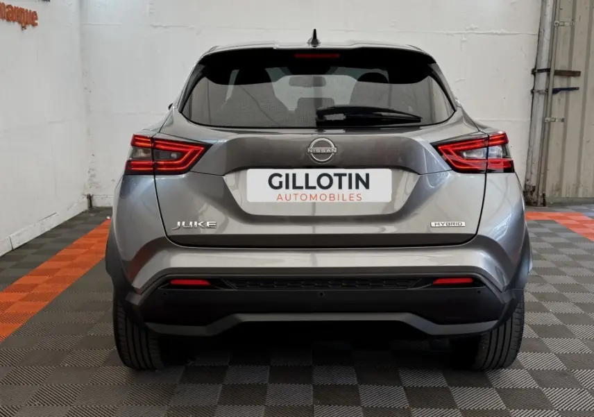 Vue arrière d'un Nissan Juke Hybrid gris foncé 2023 avec feux LED et logo Hybrid visible sur un sol à damiers noir et orange.