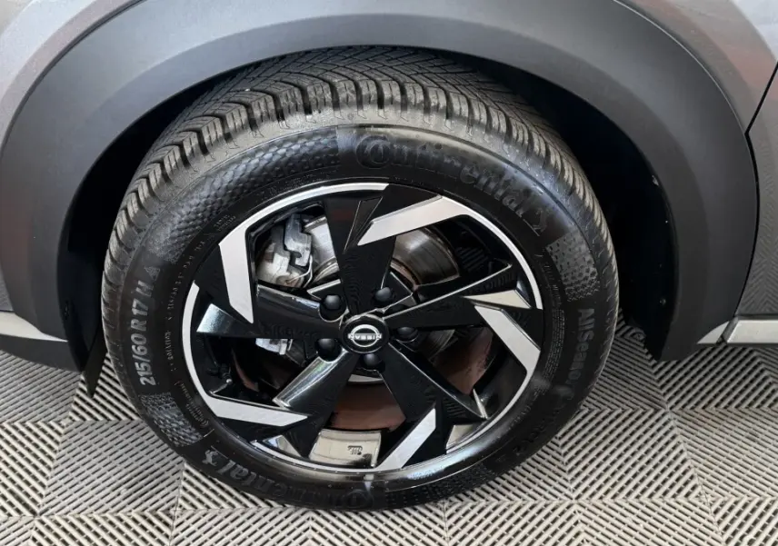 Gros plan sur la roue avant droite du Nissan Juke Hybrid gris foncé, avec jante noire et argentée au design géométrique.