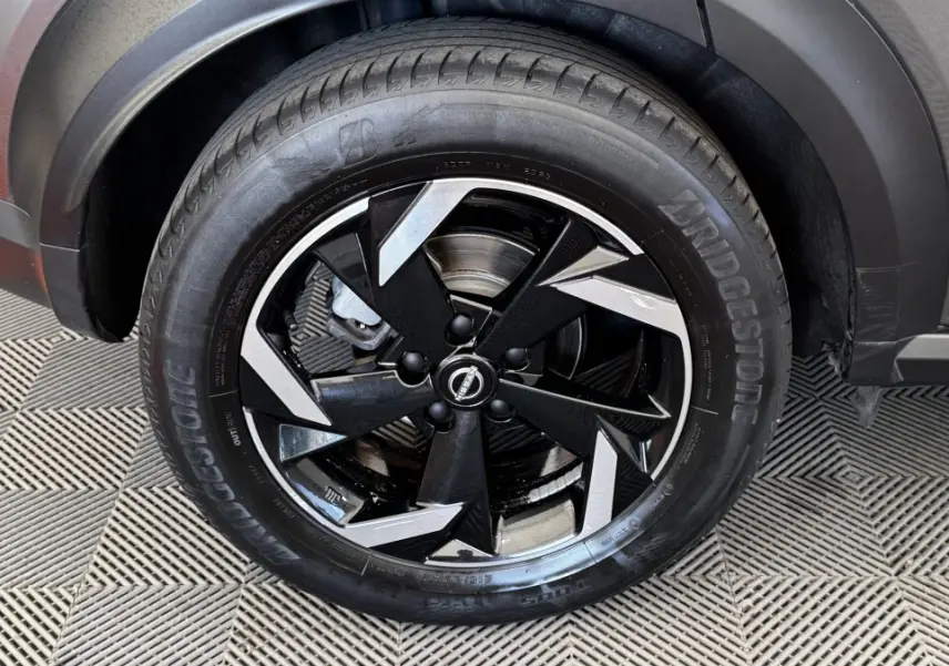 Gros plan sur la roue avant gauche du Nissan Juke Hybrid 143 Business+ gris foncé, jante alliage noire et argentée.