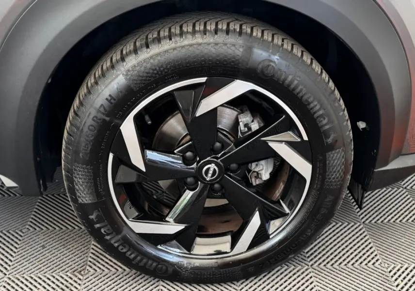 Gros plan sur la roue avant droite du Nissan Juke Hybrid gris foncé, jante alliage noire et argentée au design moderne.