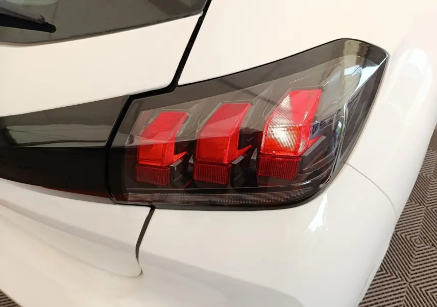 Gros plan sur le feu arrière droit rouge et noir d’une Peugeot 208 blanche, version 2023, finition Premium.
