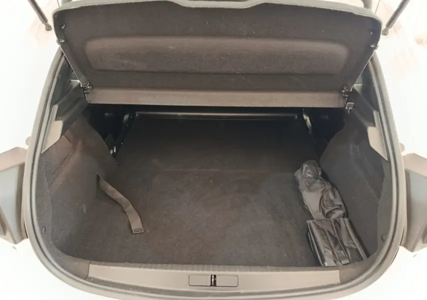 Coffre ouvert vu de dessus d’une Peugeot 208 blanche, montrant un espace de chargement vide avec housse noire sur le côté.