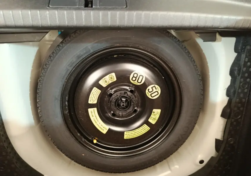 Vue rapprochée de la roue de secours noire dans le coffre blanc d’une Peugeot 208 1.5 BlueHDi 2023.